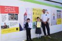 Priestley Primary School pupils Benjamin Johnston and Daisy Mae hold their original pictures, which are now displayed as big posters on hoarding at GreenSquare’s development site at Woodroff Square, alongside GreenSquare’s site manager Ian Pot